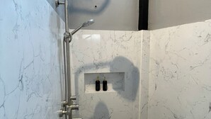 A small, modern shower with a handheld showerhead and a wall-mounted faucet.