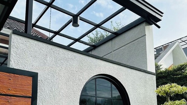 A modern building with a large circular window, a wooden panel on the left, and a small tree in the foreground.