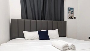 A neatly made bed with white bedding and a grey headboard, a blue pillow, and a rolled white towel on the bed.