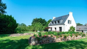 Una casa blanca con muro de piedra y jardín, rodeada de árboles.