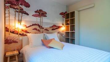 Un dormitorio con cama, almohadas, una mesita de noche, un taburete de madera y una pared decorada con un mural de temática natural.