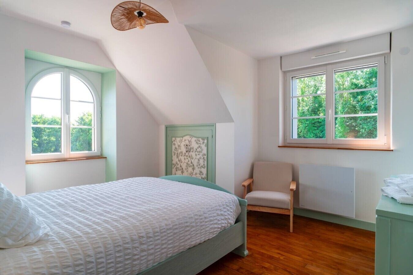 Une chambre à coucher avec un lit, une chaise, un radiateur et deux fenêtres.