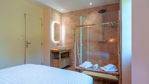 Un dormitorio con cama, baño con ducha, lavabo y espejo.