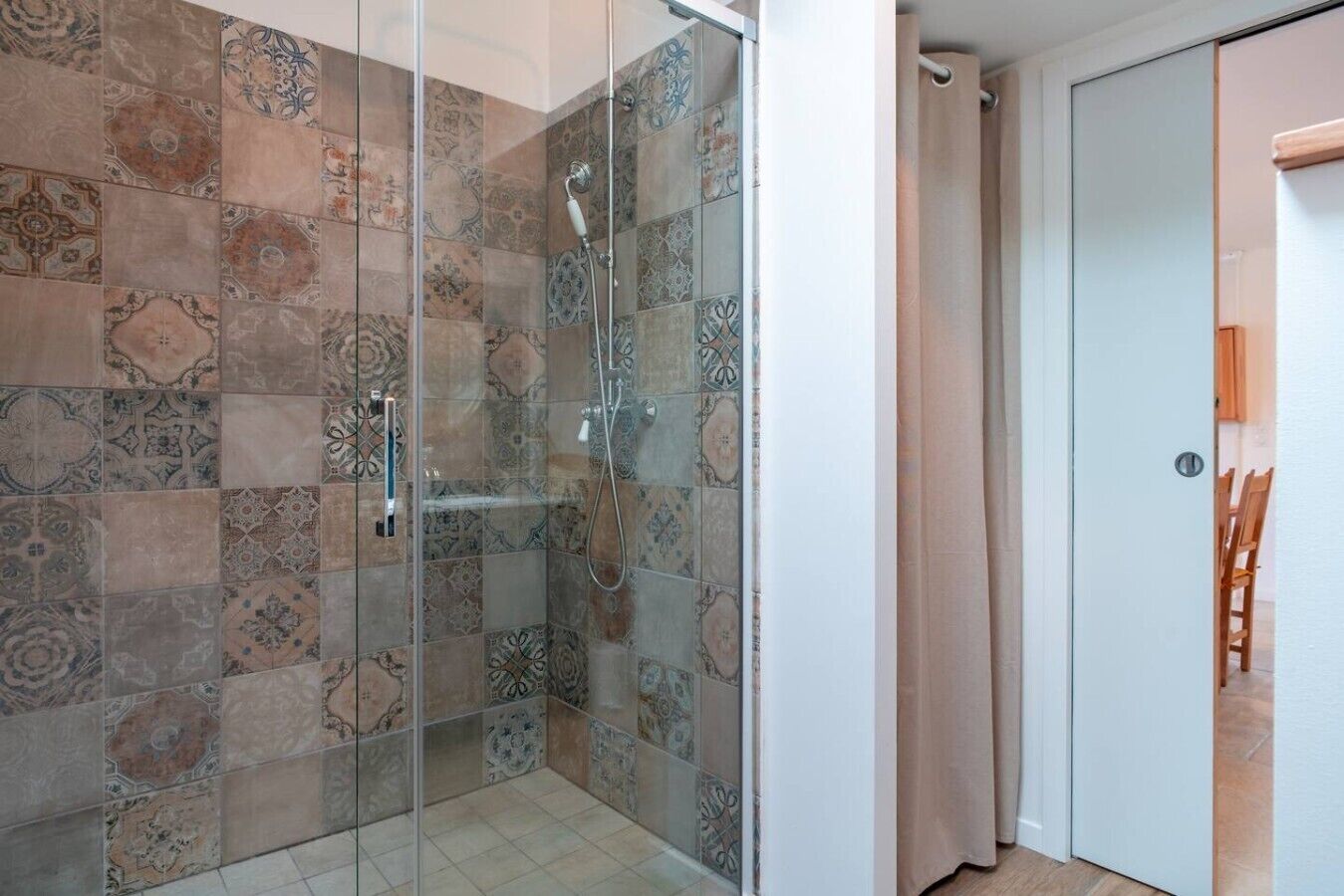 A shower with patterned tiles, a glass door, and a white door in a bathroom.