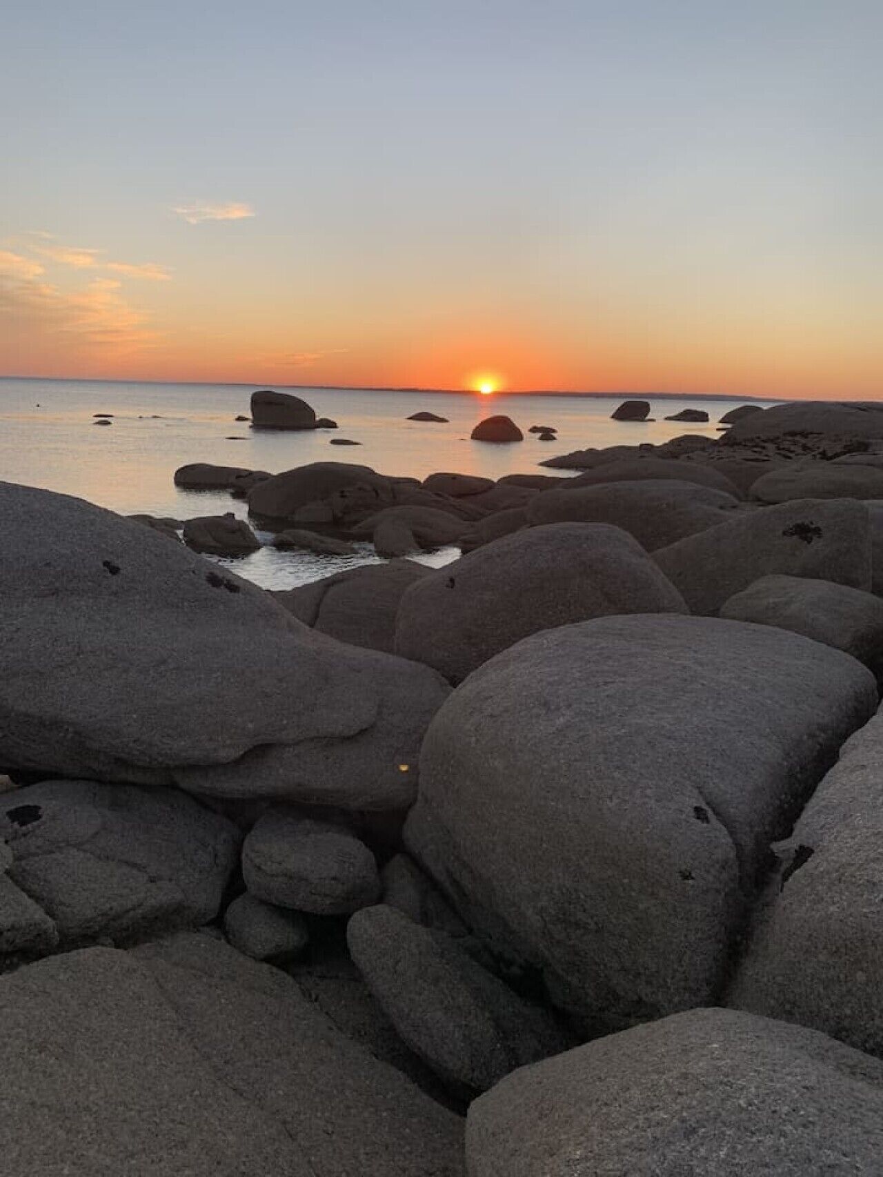 Eine felsige Küstenlinie mit großen Felsen und einem Sonnenuntergang im Hintergrund.