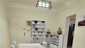 A dining area with a white table and chairs, a patterned rug, and a bookshelf with various items. - 2-bedroom apartment in marvelous Heliopolis with AC , WIFI and all needs . (Heliopolis)