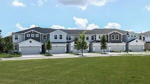 A row of townhouses with attached garages, a well-maintained lawn, and a clear sky. - Kissimmee Retreat 4BR House for 8 (Kissimmee)