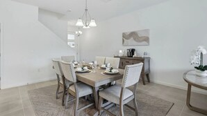 Ein Essbereich mit einem Tisch für vier Personen, Stühlen, einer Deckenleuchte, einem Gemälde an der Wand und einem kleinen Tisch mit einer Pflanze.