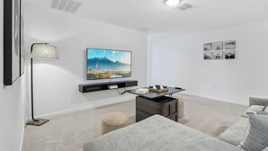 Ein modernes Wohnzimmer mit Flachbildfernseher, Stehlampe, Sofa und einem kleinen Couchtisch.