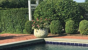 Une piscine agrémentée d’une pergola blanche et d’un grand bac à fleurs.