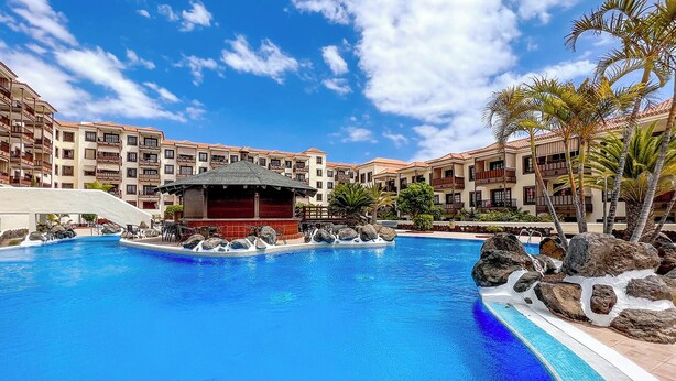 Una piscina con una formación rocosa, una zona de bar y vistas a edificios de varios pisos con balcones.