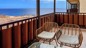 Un balcón con sillas de mimbre y una mesa de vidrio, con vista a la playa y al océano.