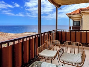 A balcony with wicker chairs and a glass table, overlooking a beach and the ocean. - Modern apartment with ocean view (Arona)