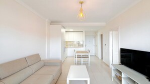 Una sala de estar moderna con un sofá, una mesa de centro, un televisor y una cocina al fondo.
