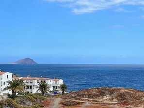 A coastal view with a white building, palm trees, and a clear blue sky. - Modern apartment with ocean view (Arona)