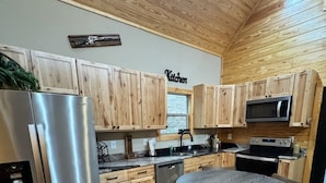 A kitchen with wooden cabinets, a stainless steel refrigerator, a microwave, a sink, and a wooden dining table with chairs. - Secluded Cabin + Private Lake Access - No Parkway Traffic - Hidden Ridge Retreat (Sevierville)