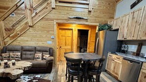 A rustic cabin interior with a wooden staircase, a dining area with a table and chairs, a sofa with decorative pillows, and a kitchen with wooden cabinets. - Secluded Cabin + Private Lake Access - No Parkway Traffic - Hidden Ridge Retreat (Sevierville)