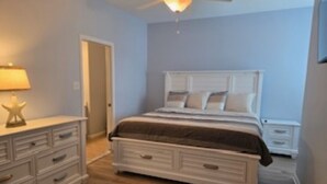 Een slaapkamer met een bed, een dressoir, nachtkastjes en een plafondventilator.