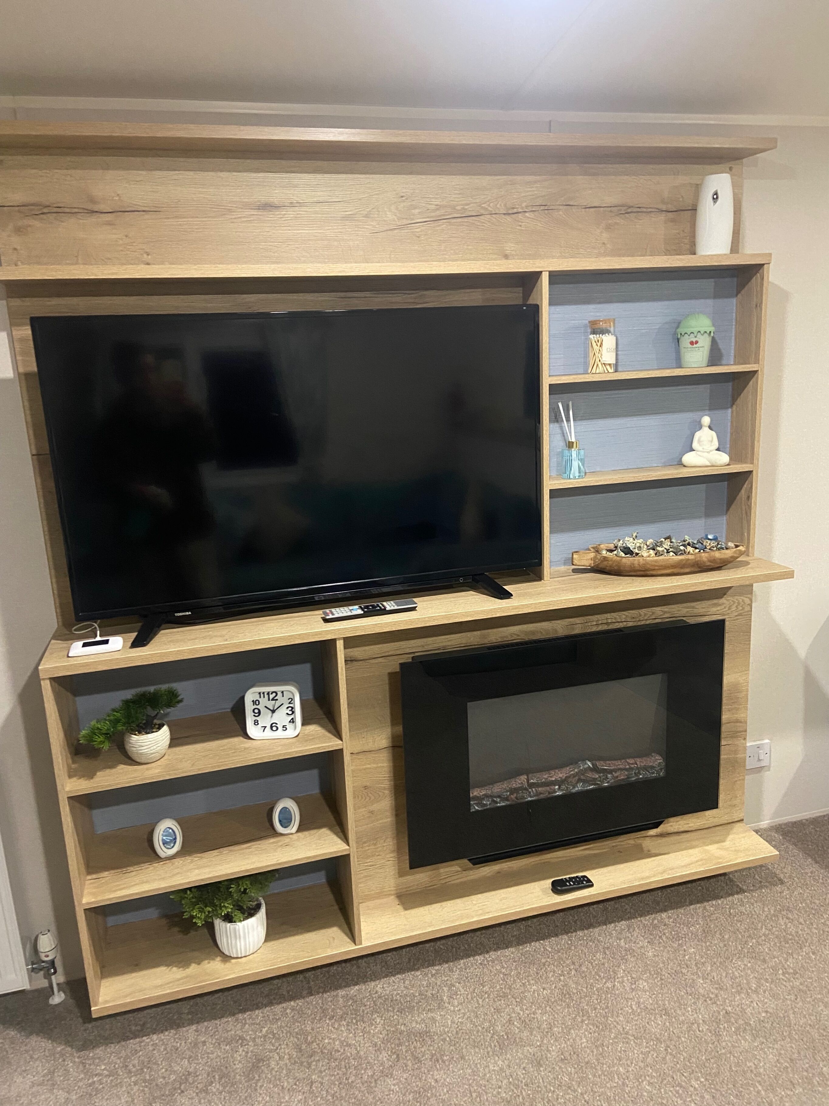 A wooden entertainment center with a flat-screen TV, a fireplace, and shelves with decorative items.