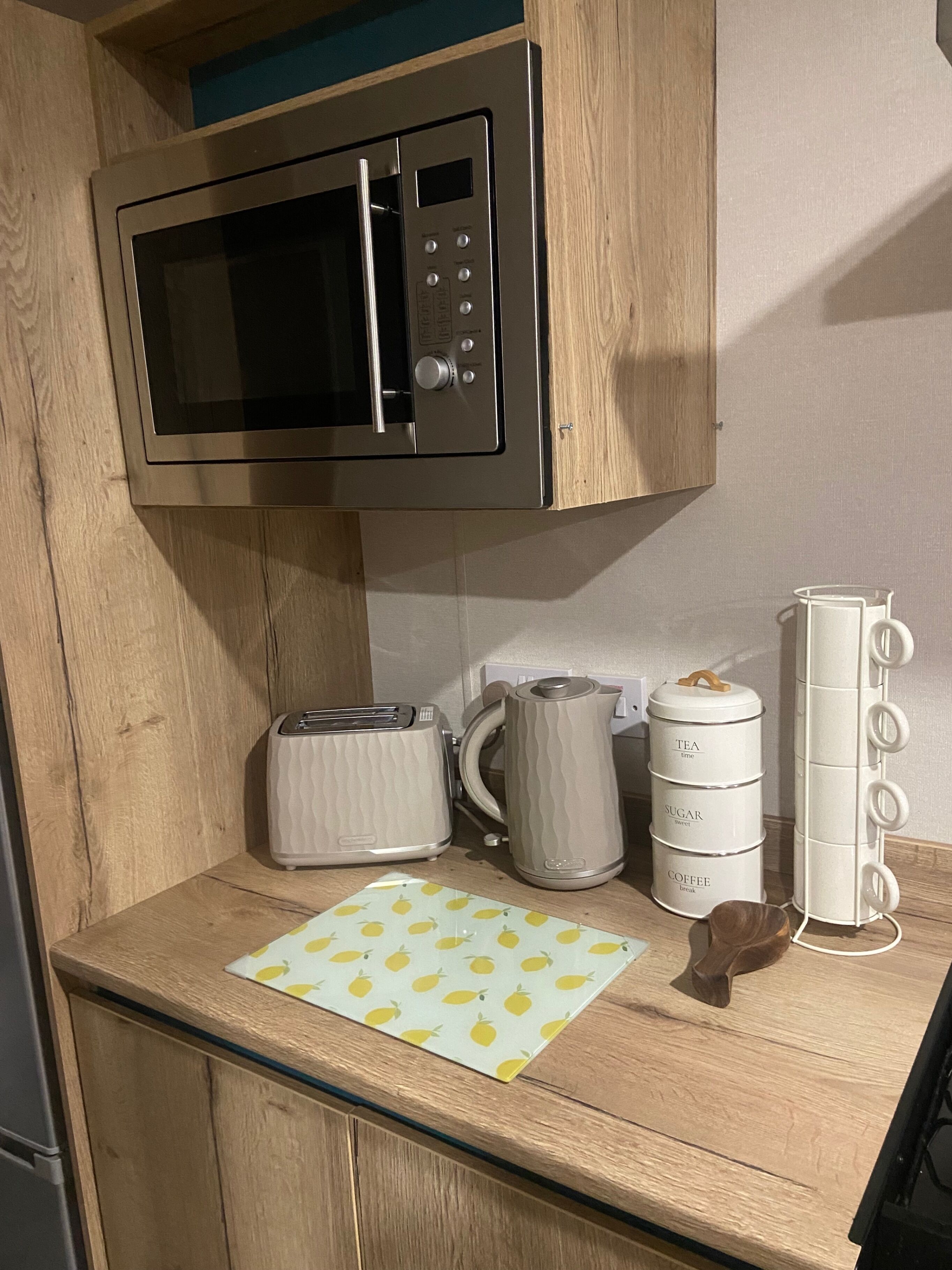 A kitchen with a microwave, toaster, kettle, and a white coffee maker with compartments labeled 'tea,' 'sugar,' and 'coffee.'