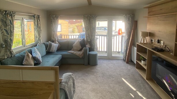 A cozy living area with a sofa, a TV, and a wooden bench. - Coworth Deluxe Cabin With Garden (Carnforth)