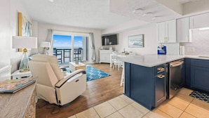 En moderne stue med sofa, spiseplads, et køkken med hvide skabe og en balkon med udsigt.