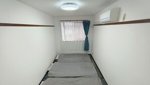 Ein schmales Zimmer mit einem Einzelbett, einem Fenster mit Vorhang, einer Klimaanlage und einem gemusterten Boden.