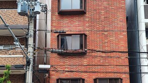 Ein mehrstöckiges Backsteingebäude mit zahlreichen Fenstern, einem erkennbaren Eingang und einem Verkaufsautomaten am Gehweg.