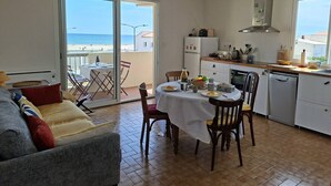 En matplats med ett bord för två personer, ett kök med diskmaskin och utsikt över havet genom en skjutdörr.