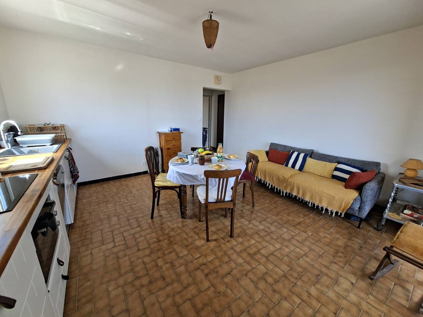 A kitchen with a dining table, chairs, and a sofa in a room with a tiled floor.