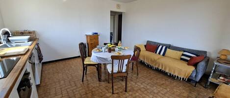 A kitchen with a dining table, chairs, and a sofa in a room with a tiled floor.