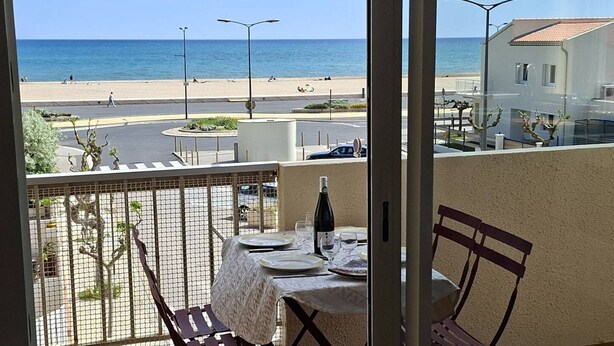 En balkong med ett bord dukat för två personer, med utsikt över en strand och en väg.