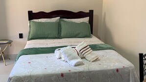 Ein ordentlich bezogenes Bett mit floralem Überwurf, zwei Kissen und einem gefalteten Handtuch.