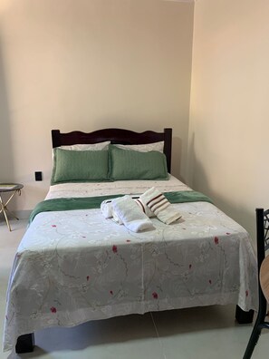 A neatly made bed with a floral bedspread, two pillows, and a folded towel. - R.E. Suites: A place of refuge, comfort, and sophistication. (Arraial do Cabo)