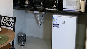 Eine kompakte Küche mit Spüle, Kaffeemaschine, Mikrowelle und kleinem Kühlschrank.
