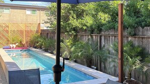 Une terrasse au bord de la piscine, avec une table, des chaises et un parasol.