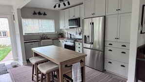 Une cuisine moderne avec des armoires blanches, des appareils en acier inoxydable, un îlot central doté de tabourets et un tapis à motifs.