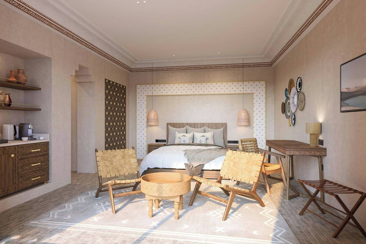 A bedroom with a bed, two chairs, a small table, a coffee machine, and shelves with decorative items.