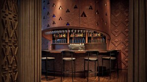 A bar area with a curved counter, bar stools, and a wall with triangular cutouts. - Amerruk, Marrakech, Autograph Collection (Marrakech)