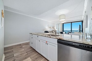 Eine moderne Küche mit Spülmaschine, einer Marmorarbeitsplatte und Blick auf den Balkon.