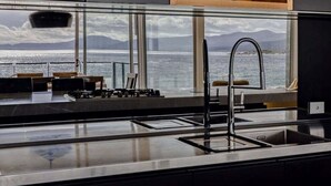 A modern kitchen with a large window overlooking a body of water and mountains.