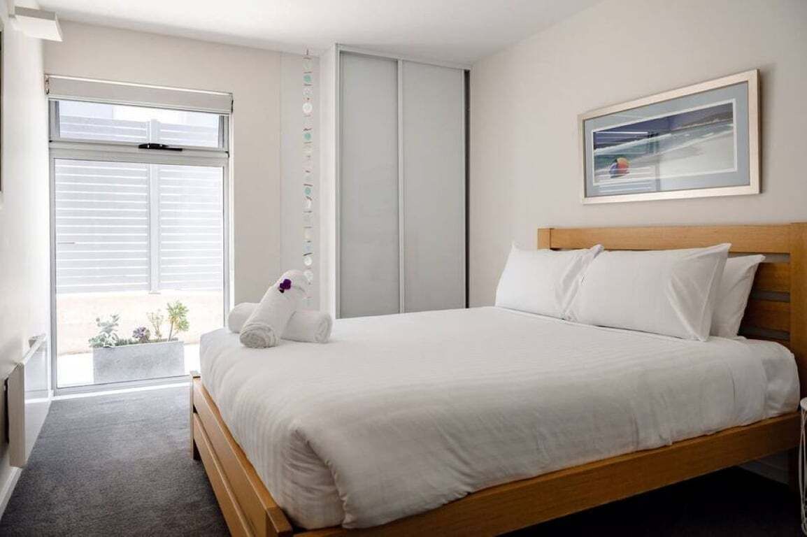 A hotel room with a bed, a window, a door, and a framed picture on the wall.