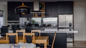 A modern kitchen with a central island, black cabinets, and a dining area with wooden furniture.