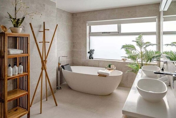 Une salle de bain moderne avec une baignoire sur pieds, des étagères en bois et des plantes en pot.