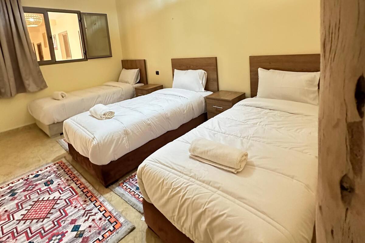 A hotel room with two beds, a patterned rug, a wooden headboard, and a ceiling light fixture.