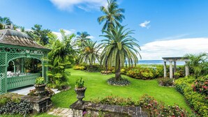 Un rigoglioso giardino con palme, un gazebo e vista sull'oceano.