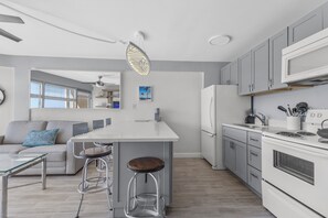 A modern kitchen with a central island, grey cabinets, and stainless steel appliances. - Cozy, updated 1-bedroom condo steps from the ocean (Daytona Beach)