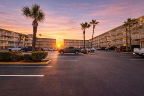 A hotel with multiple floors, a parking lot, and palm trees. - Cozy, updated 1-bedroom condo steps from the ocean (Daytona Beach)