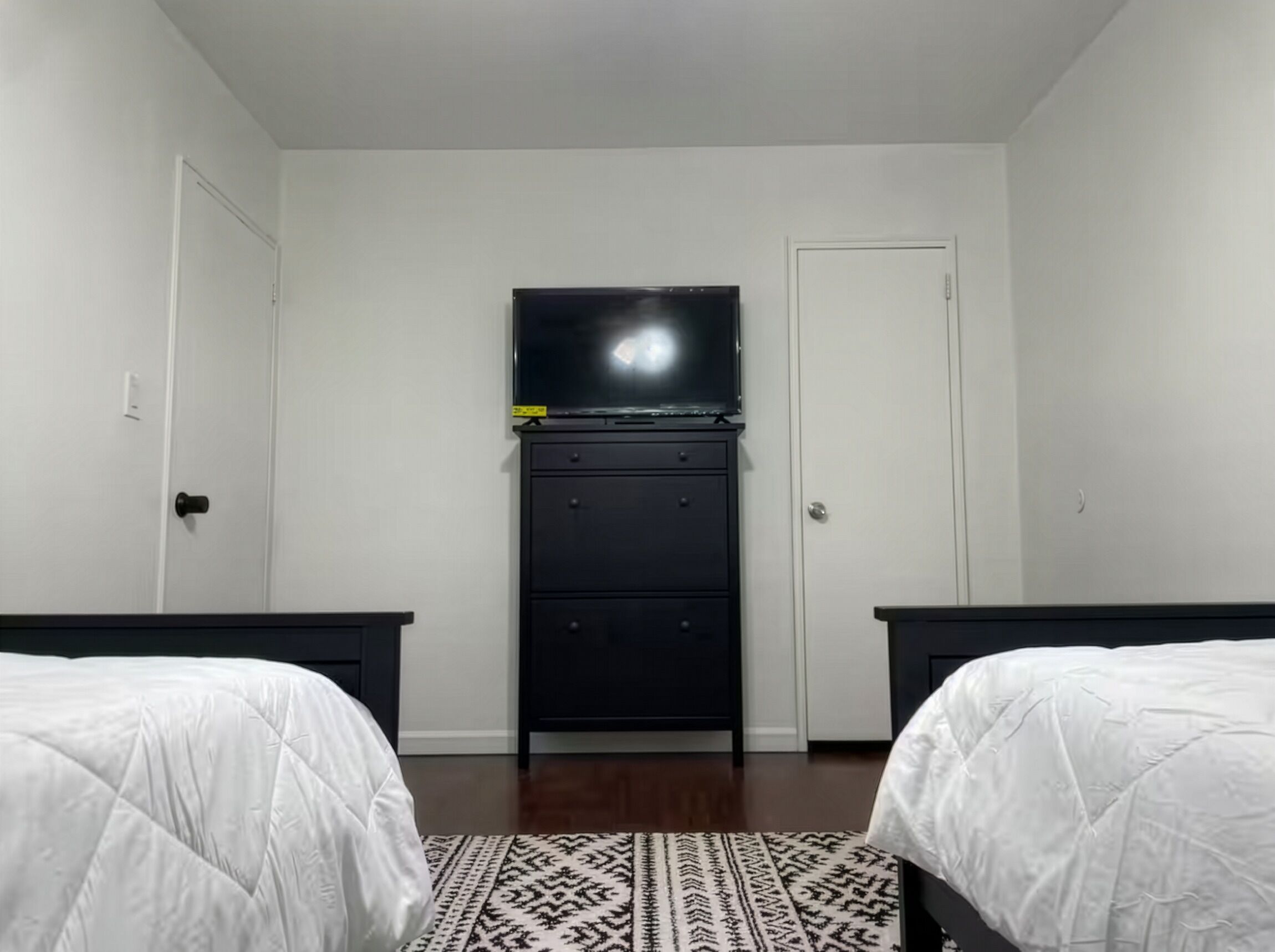 A bedroom with two beds, a TV on a stand, and a patterned rug.