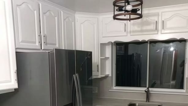 Una cocina con armarios blancos, un refrigerador de acero inoxidable, un ventanal sobre el fregadero y piso de mármol.
